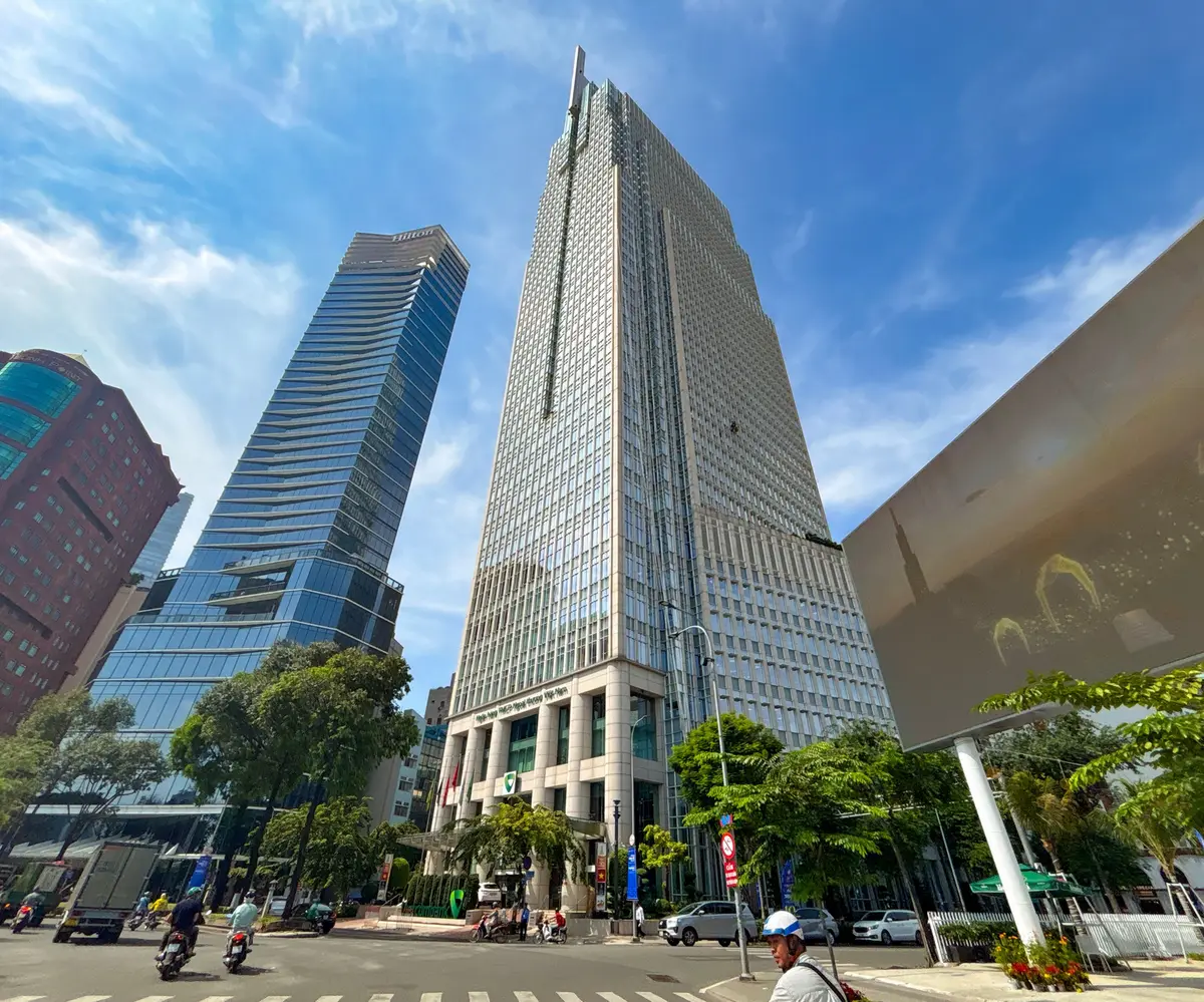 Vietcombank Tower seen from the street, a tall glass tower with low trees at its base.