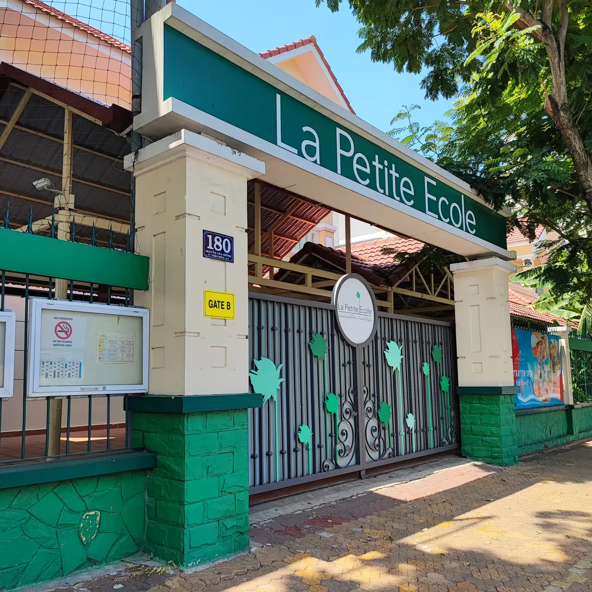 Green La Petite Ecole sign above a metal gate with leaf cut-outs between two pillars