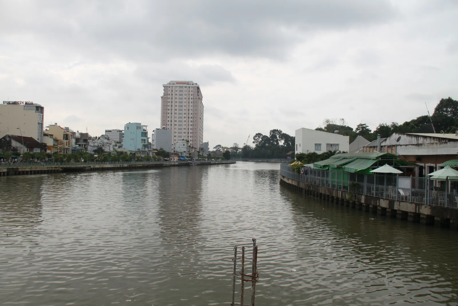 Brown canal between houses and walkways with a tall building in the distance