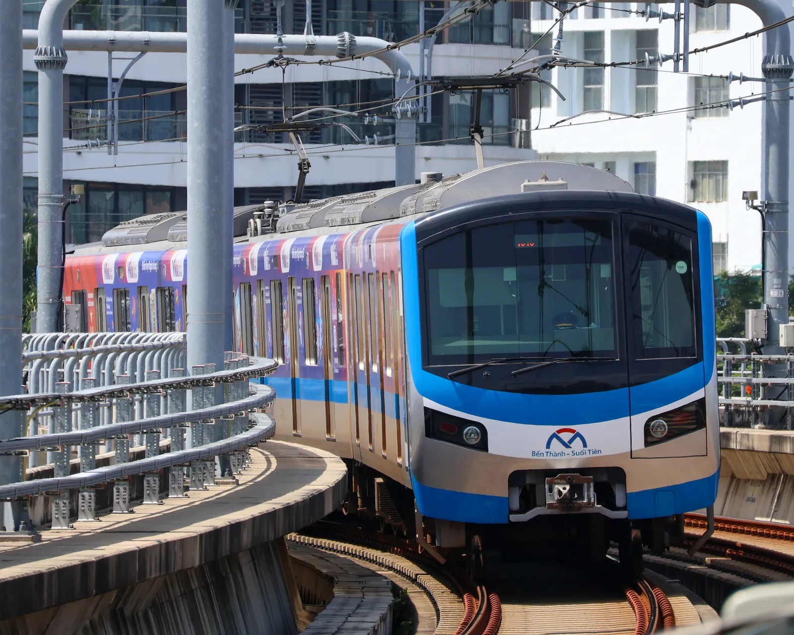 Blue and white metro train rounding a curve beside a station and a steel fence