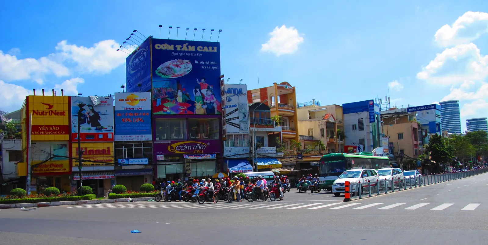 Busy road junction with motorbikes waiting at a crossing and large shop billboards