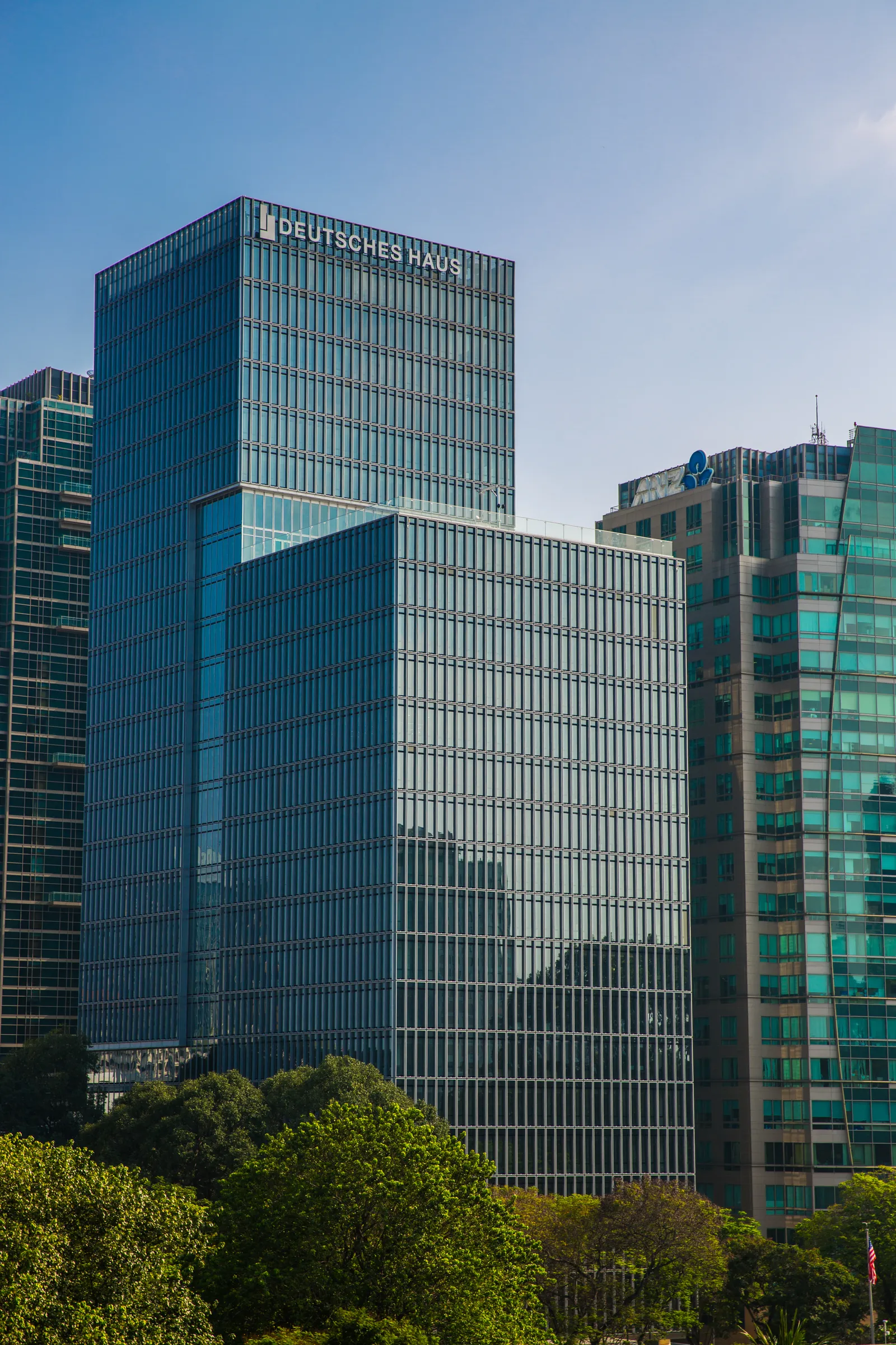 Tall glass office tower with the Deutsches Haus sign near the top, seen from below among trees