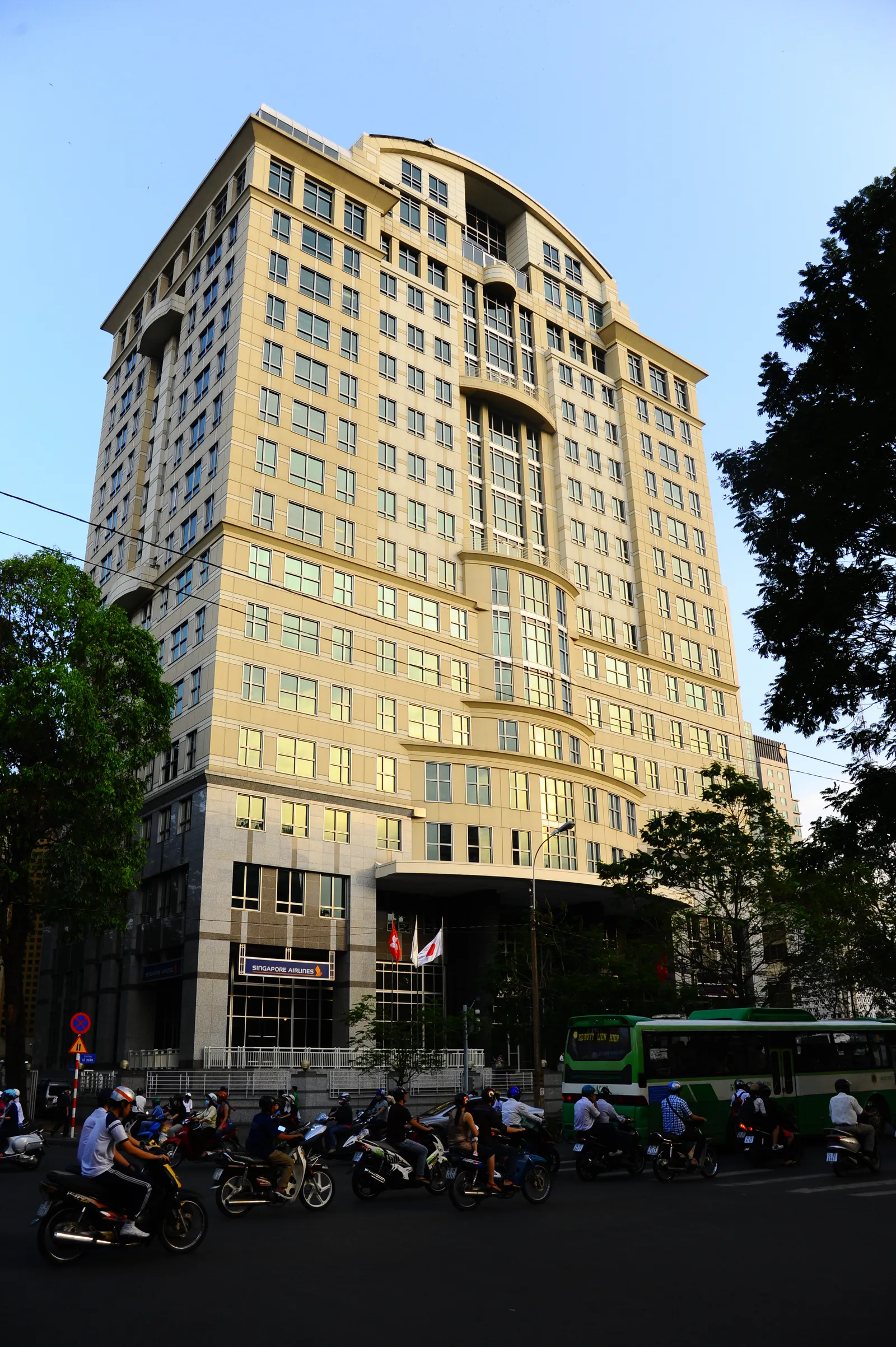 Tall cream and gold office tower on a street corner with motorbikes passing in front