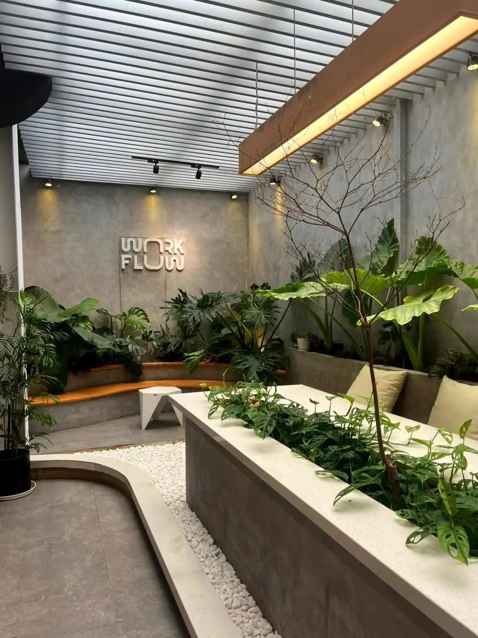 Concrete wall with a logo above a planted garden bed and cushioned seating