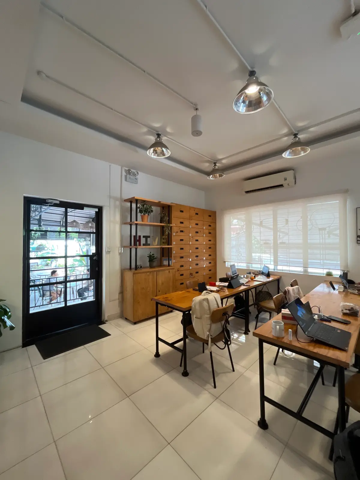 Wooden desks with laptops beside a glass door and a wall of wooden drawers