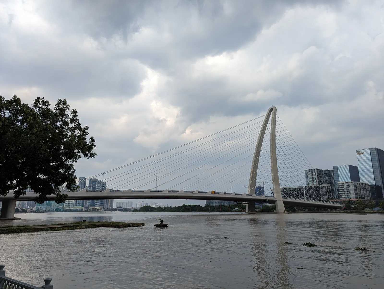 Cable-stayed bridge with a tall arch over a wide brown river under a cloudy sky