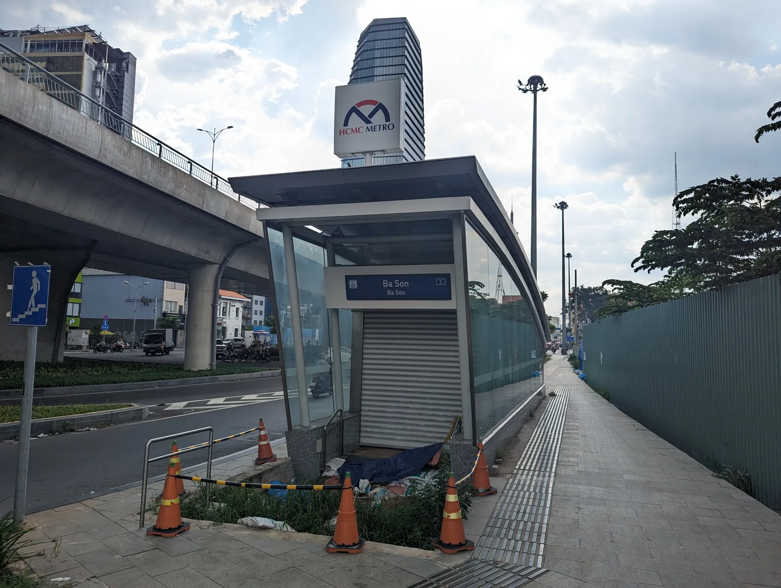 Glass-roofed metro station entrance beside an elevated road with a tower behind