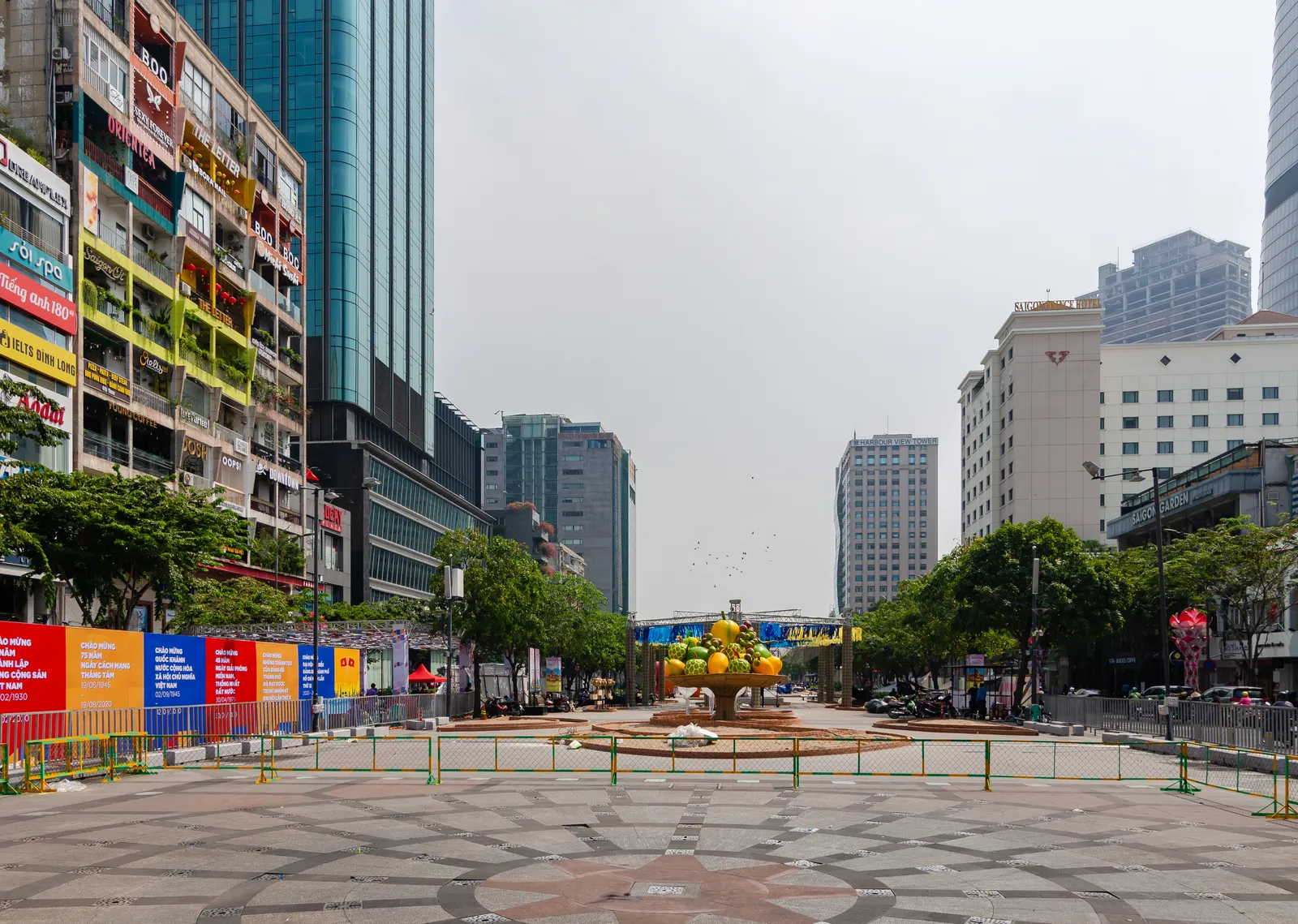 Wide paved pedestrian boulevard with colourful shopfronts and tall towers in the distance