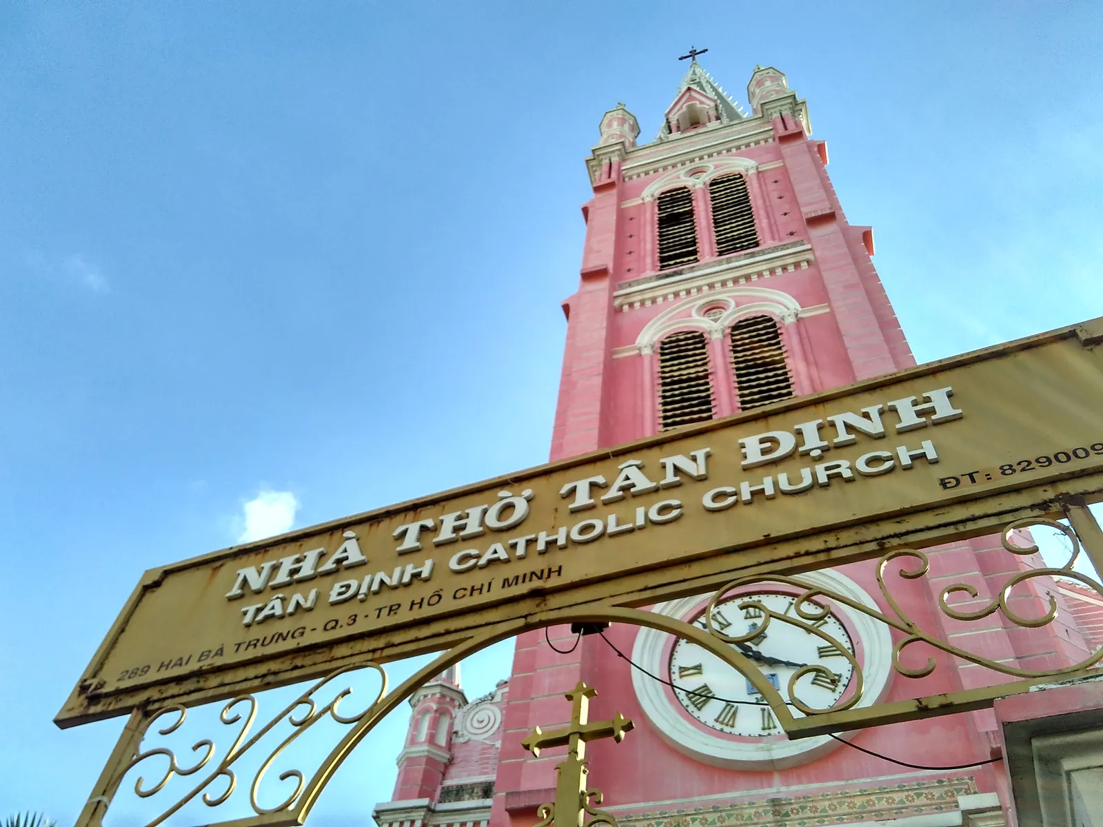 Pink church bell tower behind a gold name sign and an iron gate