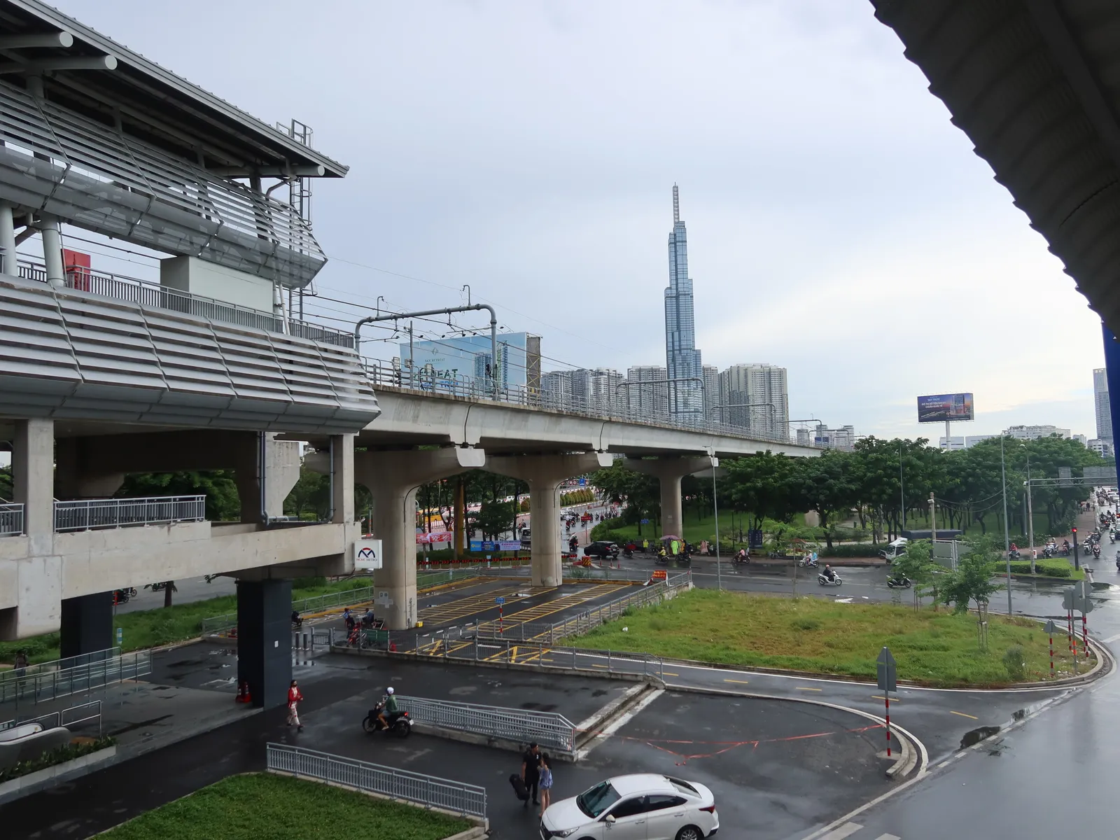 Elevated metro station and tracks beside a road with a tall tower in the distance