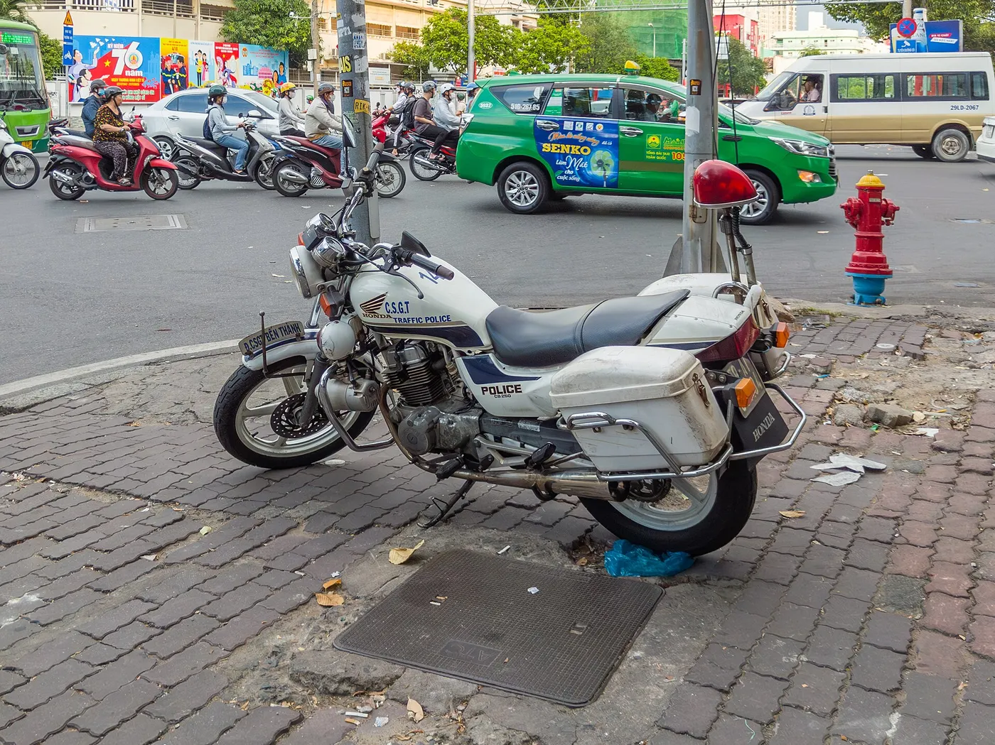 White police motorbike parked on a brick pavement beside a street in Ho Chi Minh City