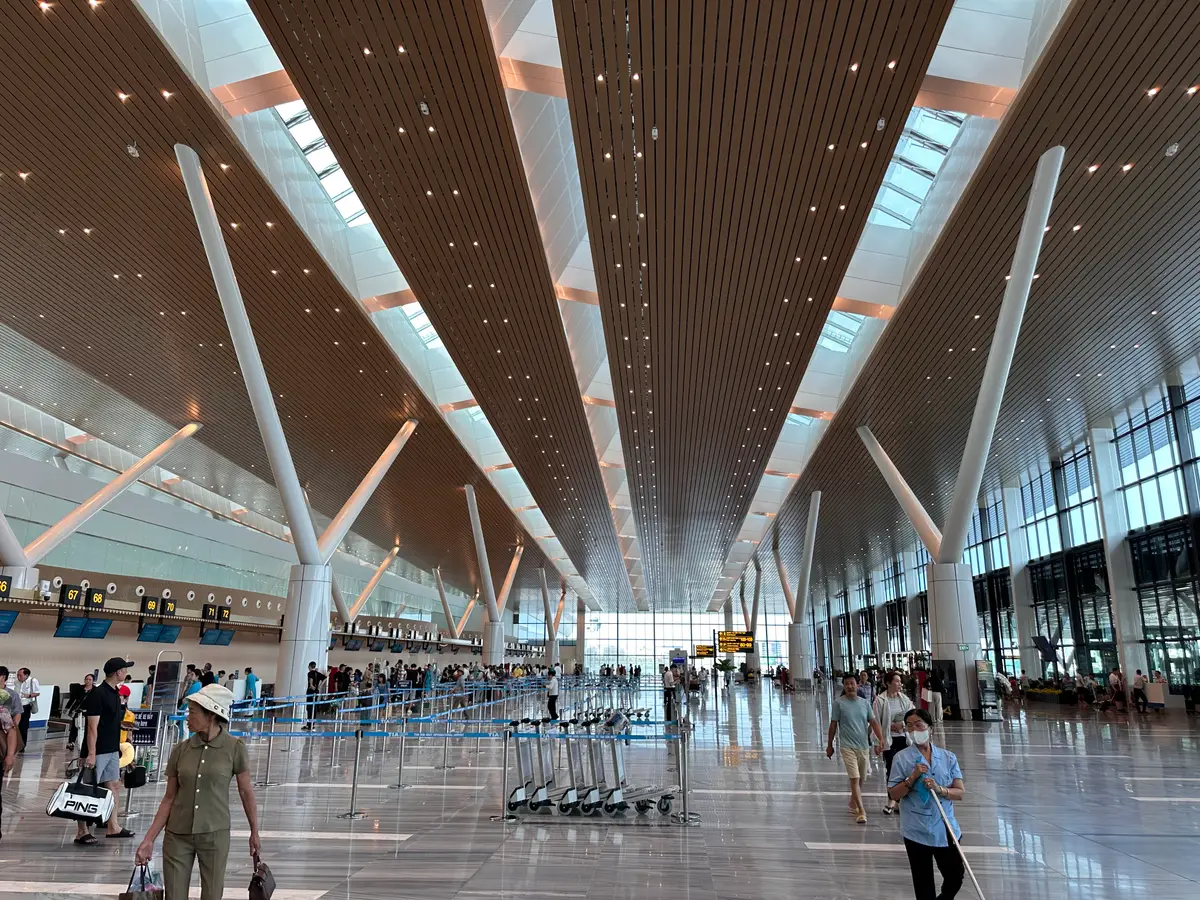 Wide terminal hall at Tan Son Nhat International Airport with a high ceiling, white columns and a few travellers with luggage trolleys