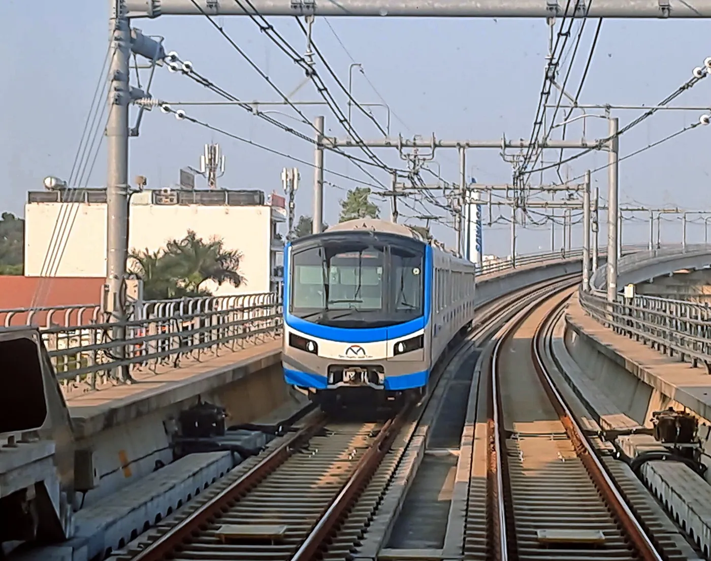 Blue and white metro train approaching on elevated tracks between overhead wires