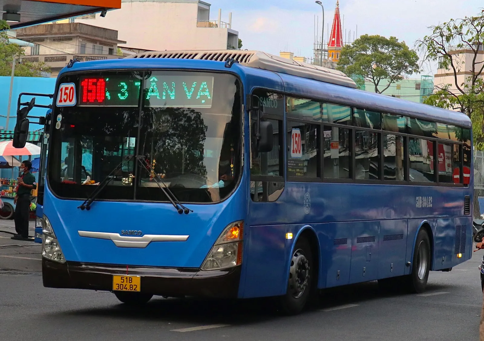 Blue city bus with a red route display at a stop on a city street