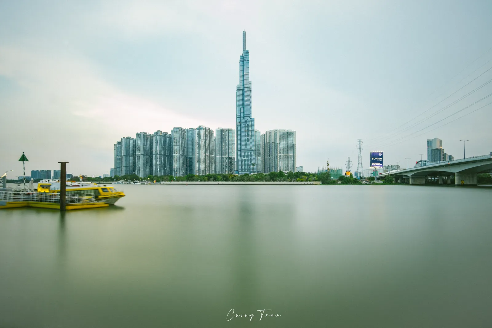 Tall skyscraper across a calm river with a small yellow passenger boat at the left edge