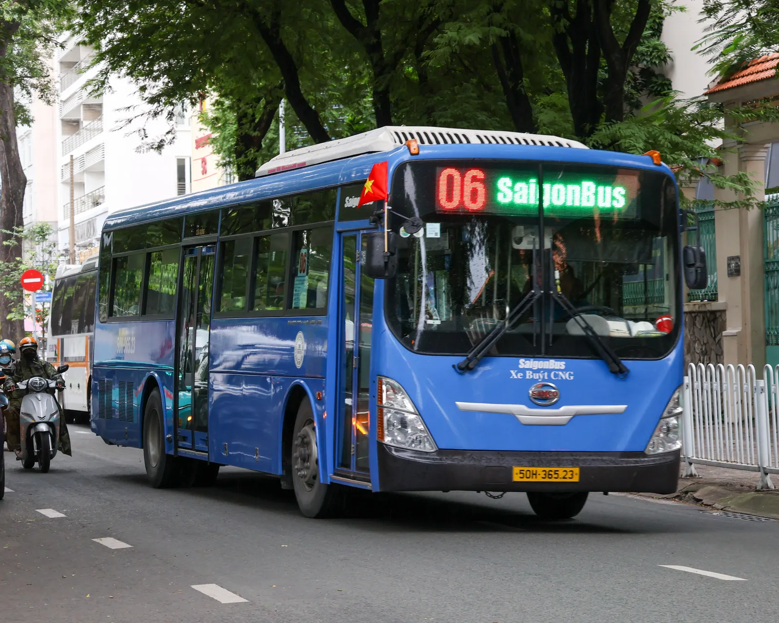 Blue city bus with a lit route sign driving along a street past motorbikes