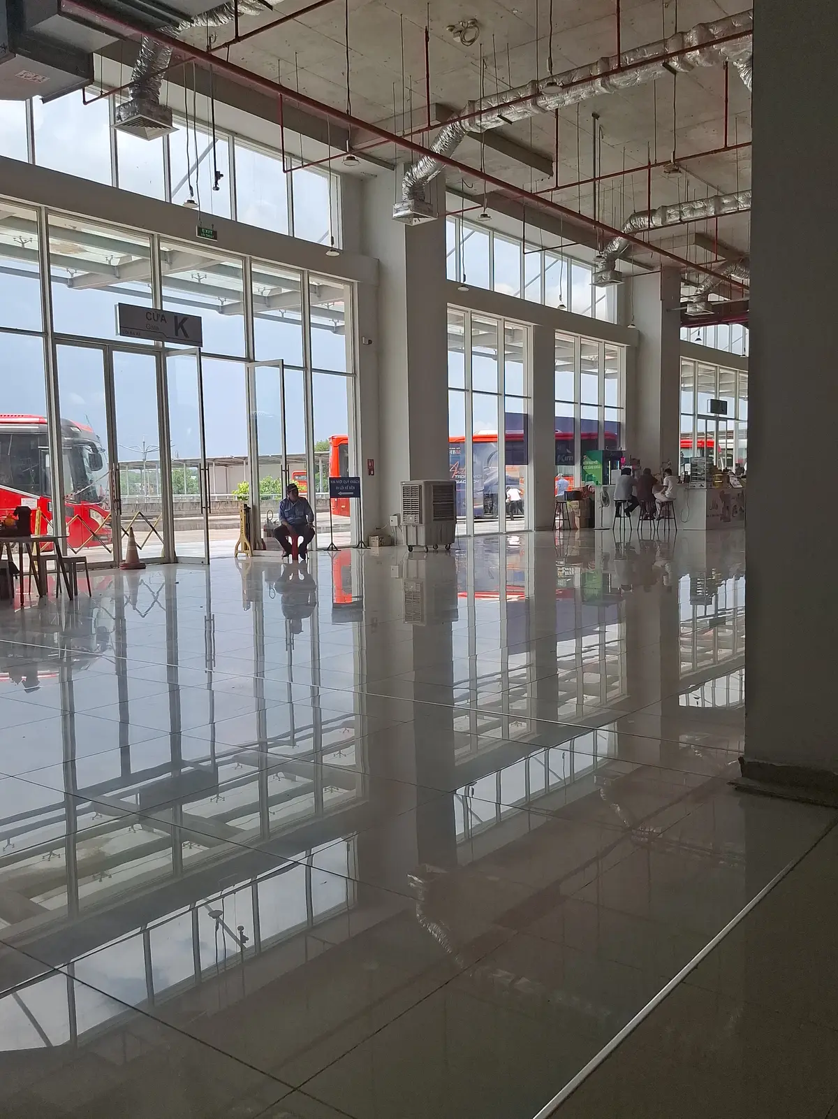 Wide glass-walled station hall with a polished floor and coaches parked outside