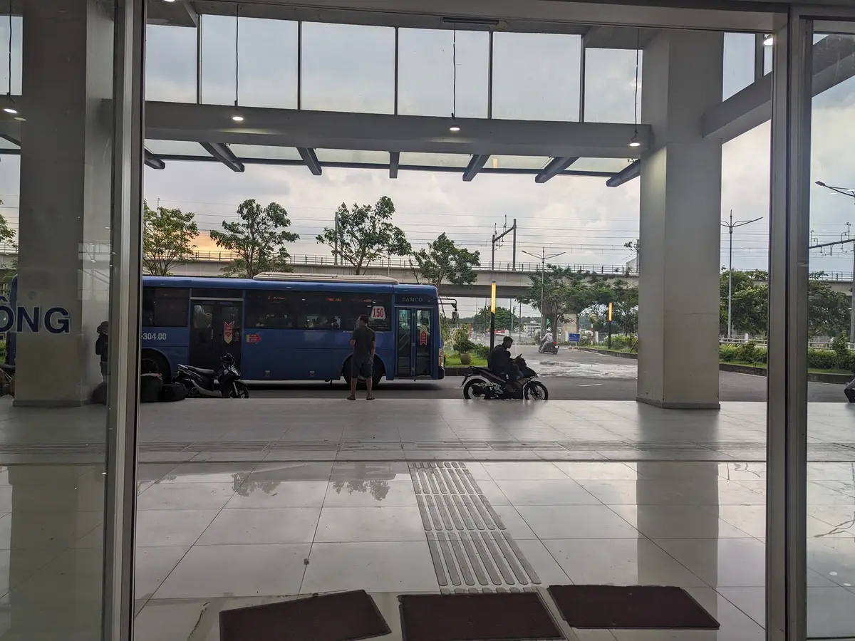 Blue bus outside the glass doors of the station hall with a covered walkway in front