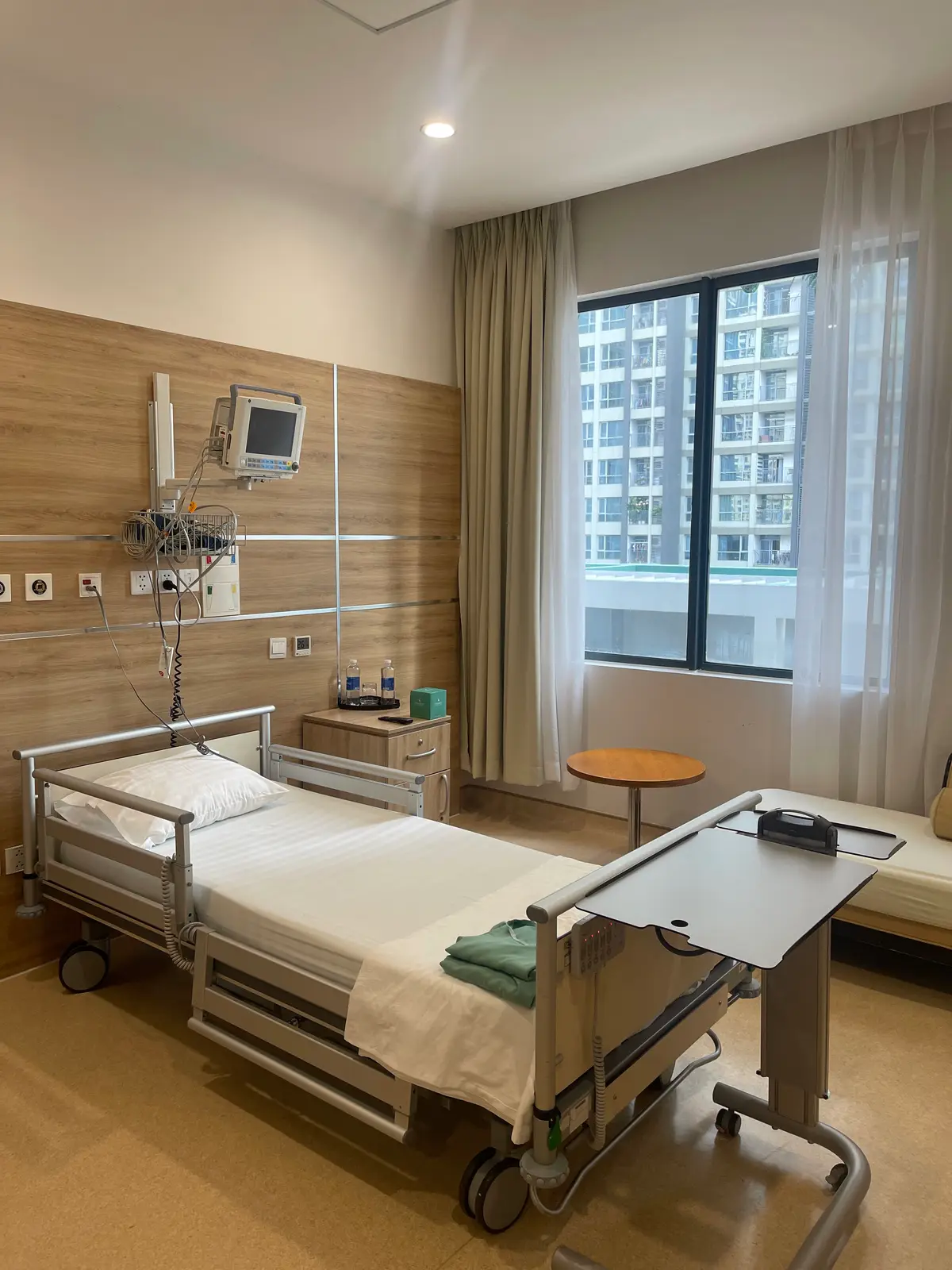 Single patient room at Vinmec Central Park with a hospital bed, monitor and window onto apartment towers.