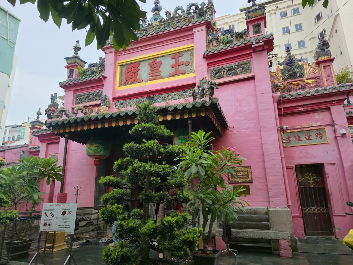 Pink temple facade with green roof tiles seen through a pine tree