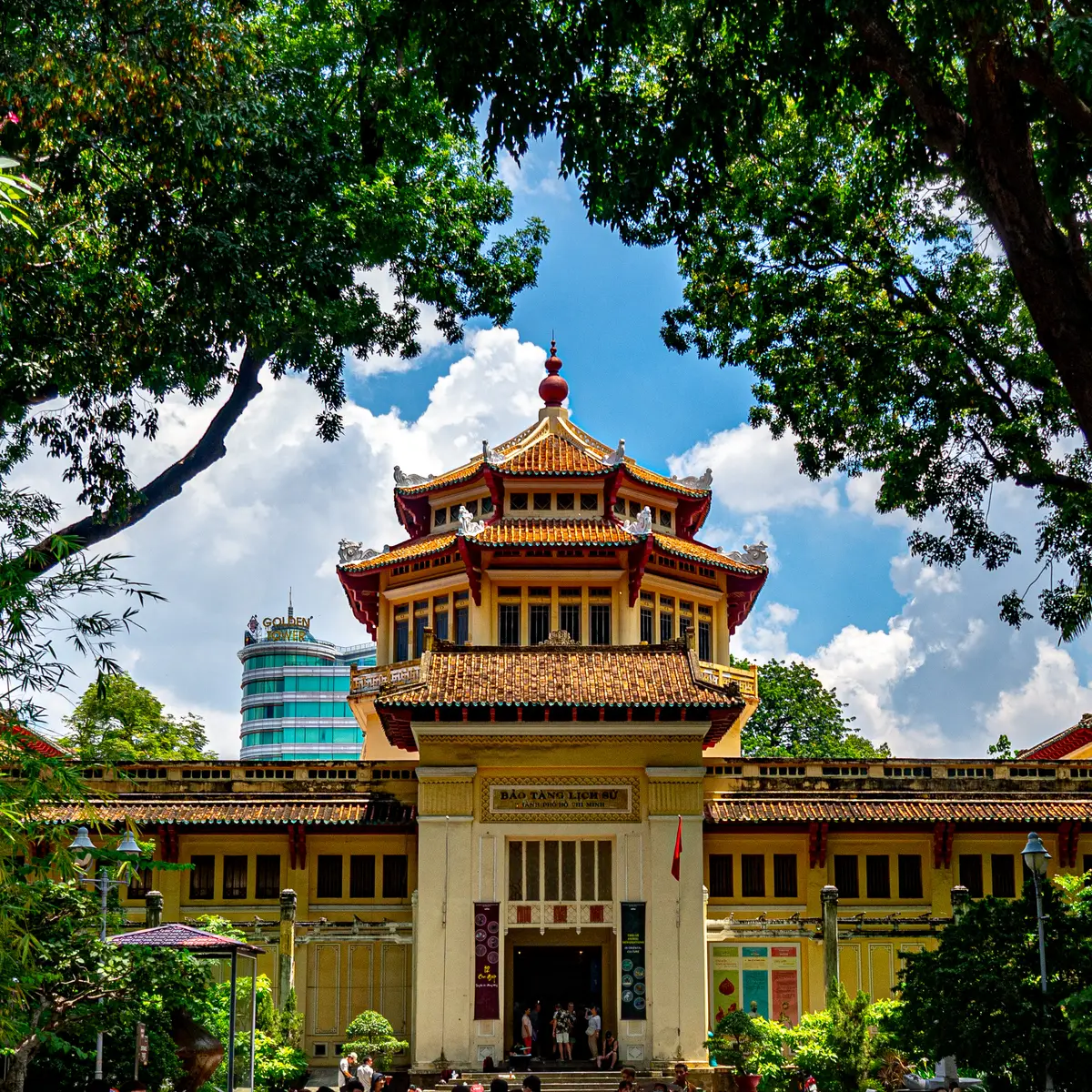 Yellow building with a pagoda-style red tiled roof tower seen from below through tree branches