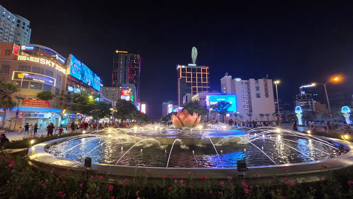 Lit fountain shaped like a lotus flower at night with illuminated buildings behind