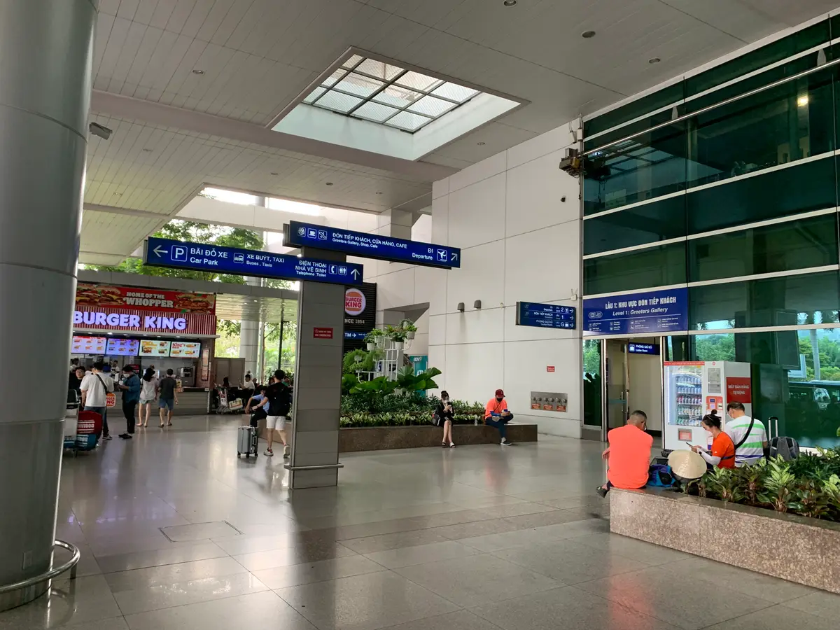 Airport hall with overhead direction signs, a skylight, indoor plants and a fast-food counter