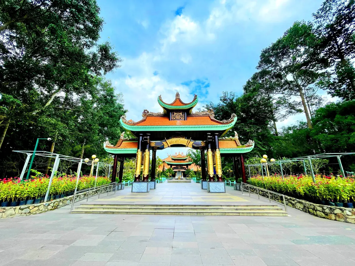 Temple-style gate with red tiled roofs and flower beds across a paved square under trees