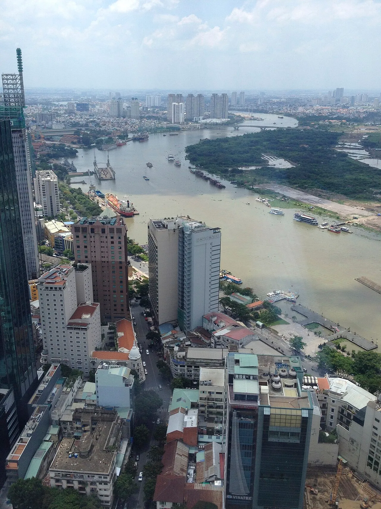 View from a high floor over city blocks and a wide bend of the Saigon River with boats and green land beyond