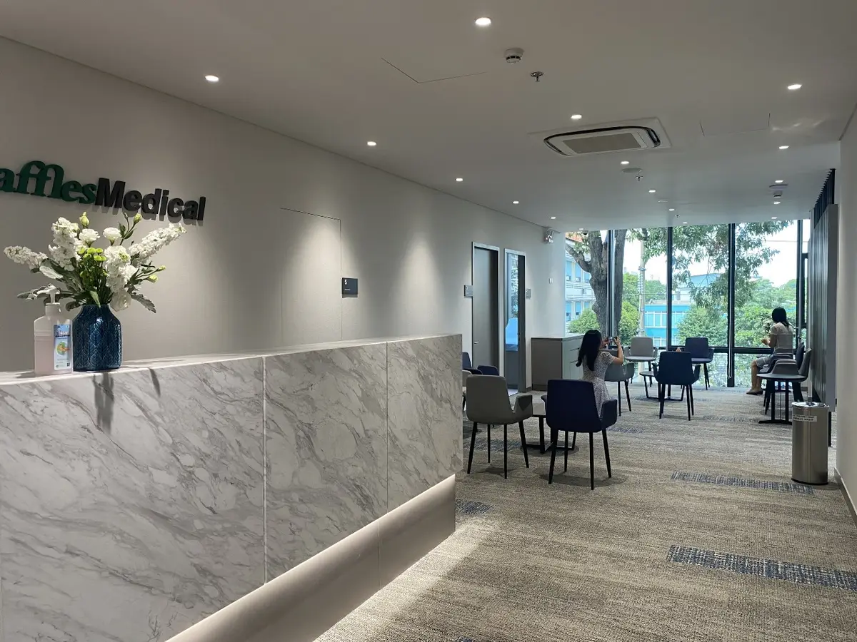 Marble reception desk with the Raffles Medical logo and flowers at the clinic.
