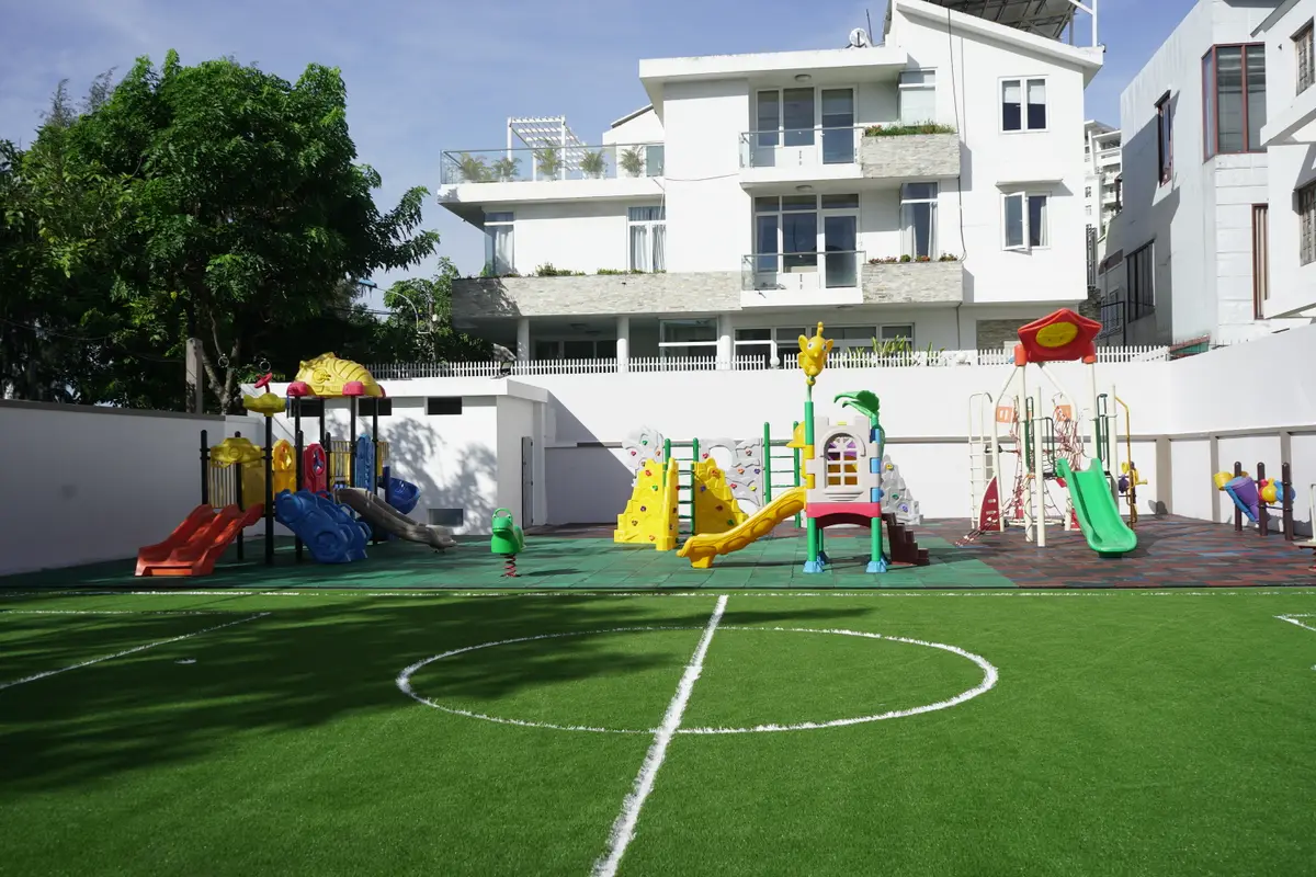 Artificial turf play area with slides and a painted circle, school buildings behind
