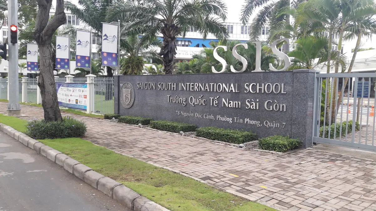 Stone name sign with the school initials beside a paved path
