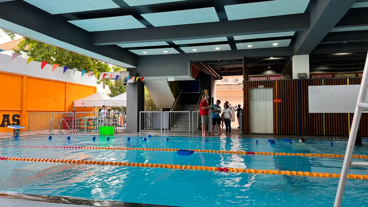 Outdoor swimming pool with orange and yellow lane ropes beneath a concrete roof