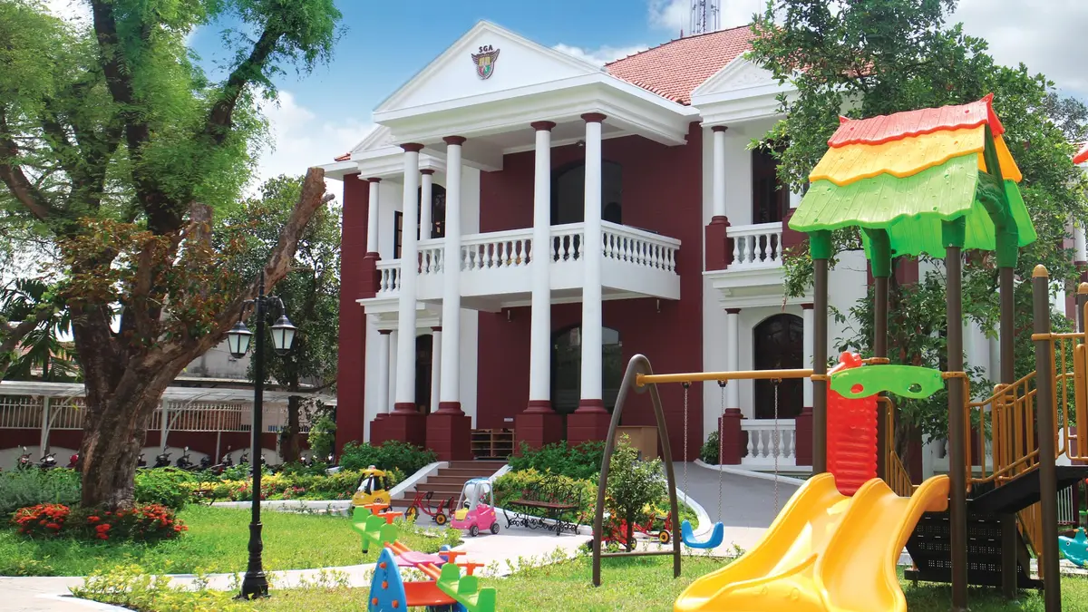 White colonnaded building with red walls behind a lawn and a play slide