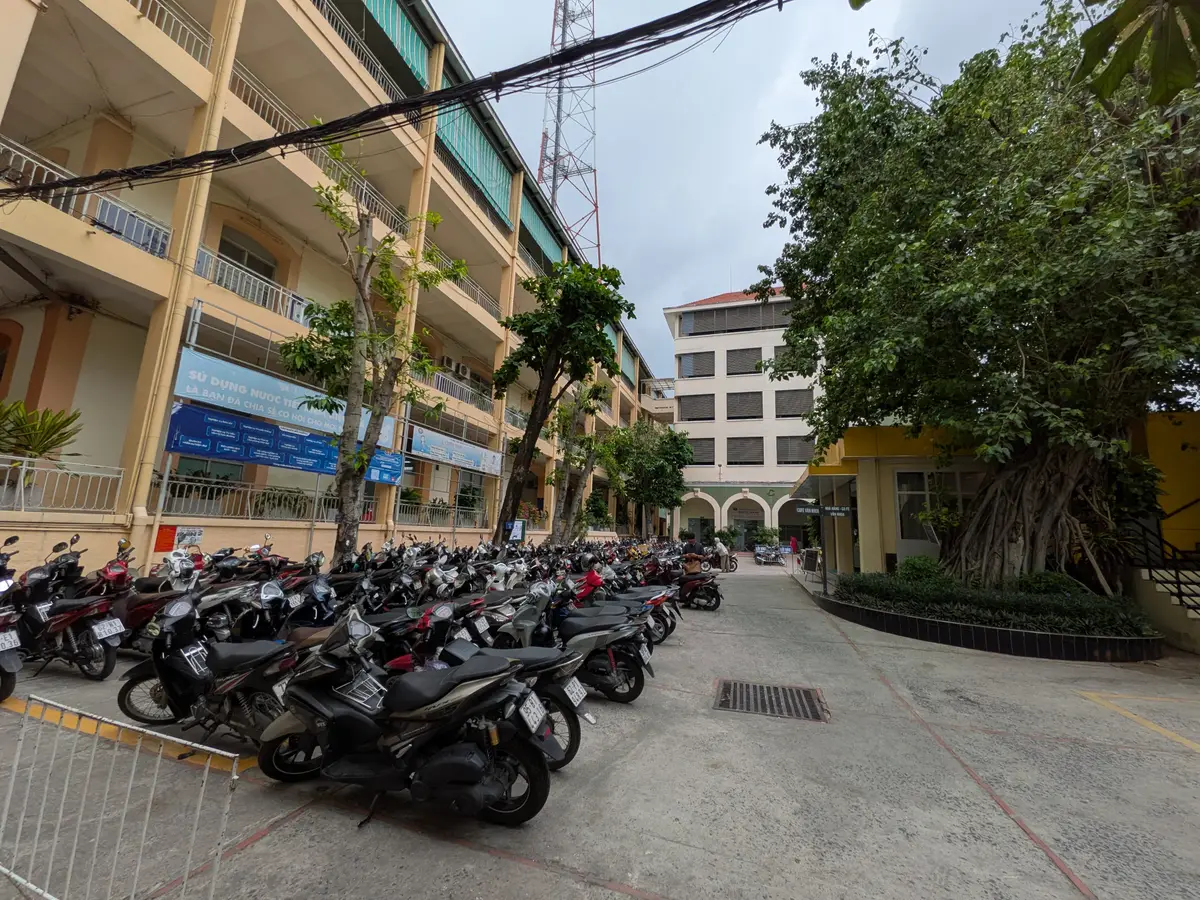 Yellow school buildings beside a courtyard with parked motorbikes under trees