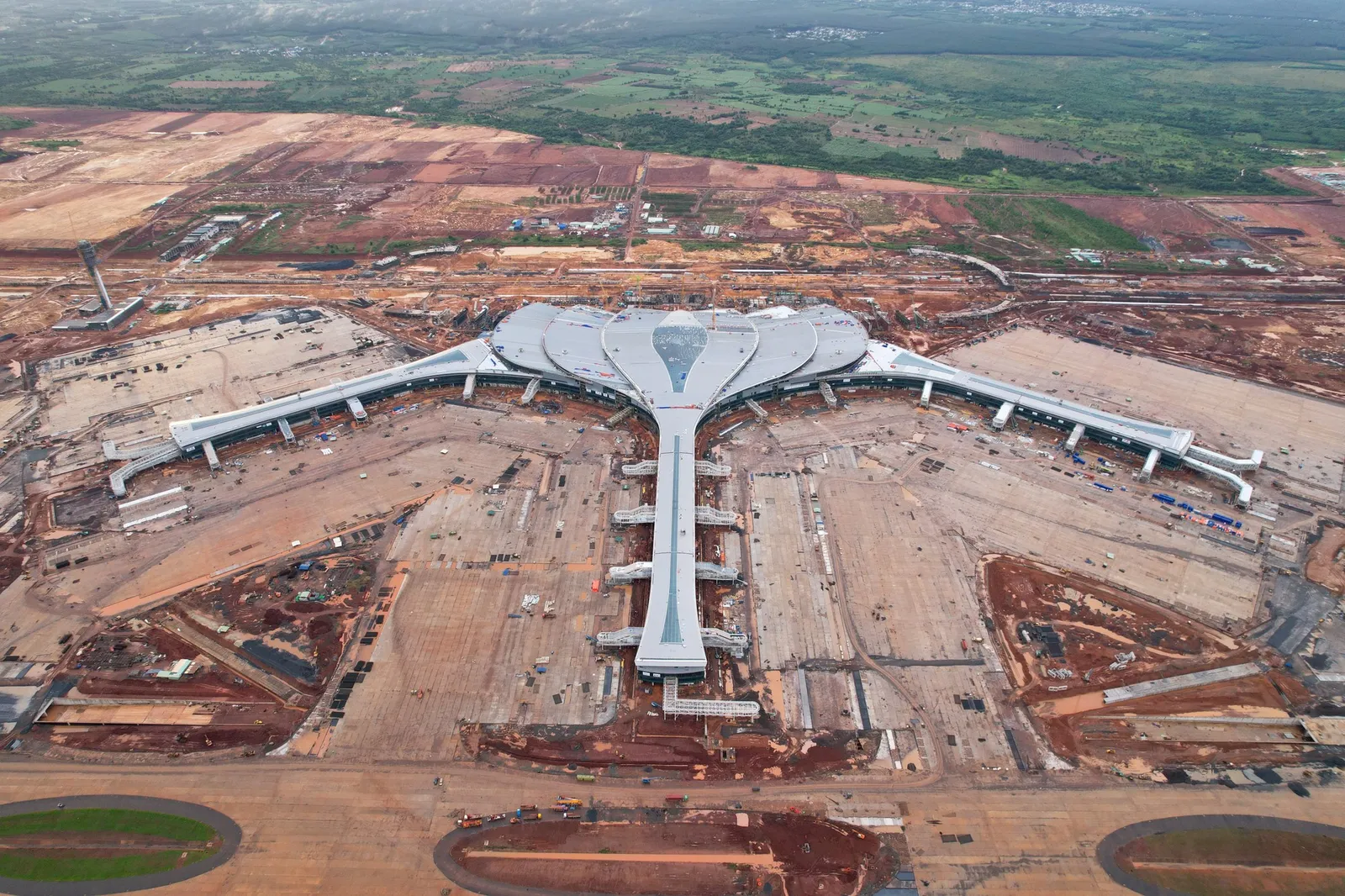 Aerial view of a large Y-shaped airport terminal with long wings surrounded by red earth and airfield