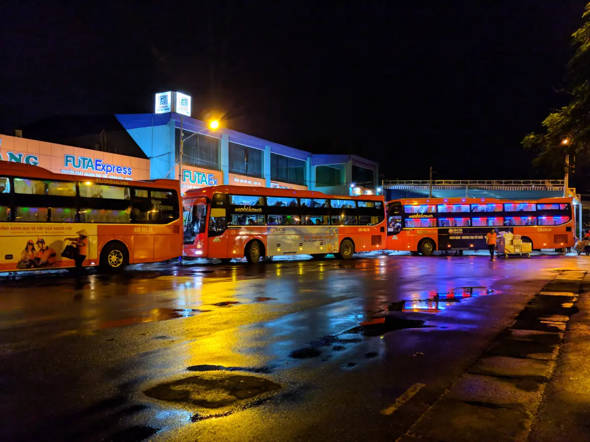 Orange and red coaches parked on a wet forecourt at night under station lights
