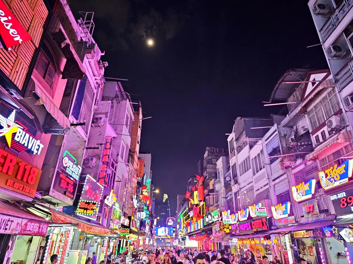 Narrow street at night packed with bar and restaurant signs in pink and purple light