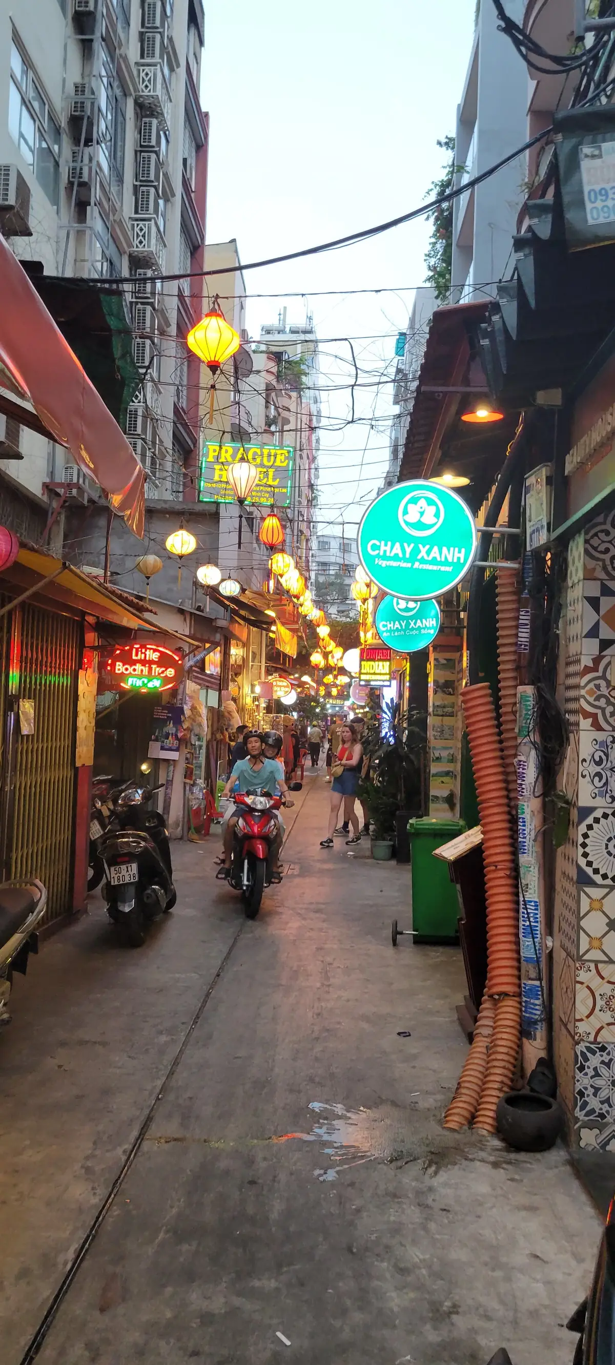 Side lane with hanging lanterns, a Chay Xanh sign and a motorbike rider at night