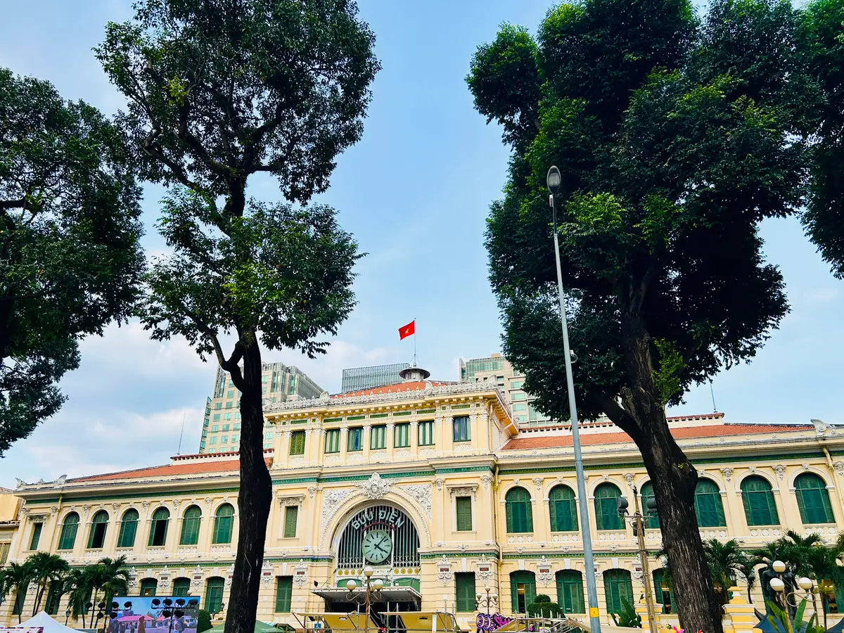 Yellow post office building with a red flag seen through large green trees