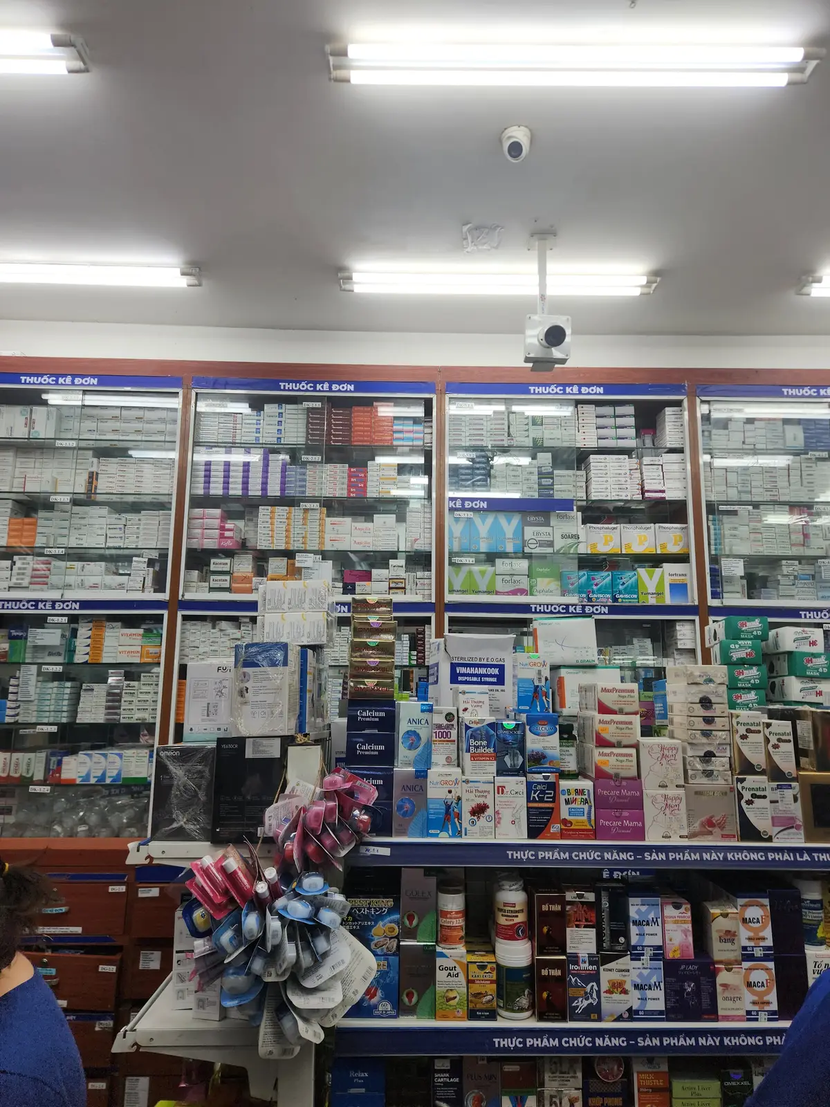 Wall of shelves with boxed medicines under signs marked as prescription drugs in a Long Chau pharmacy.