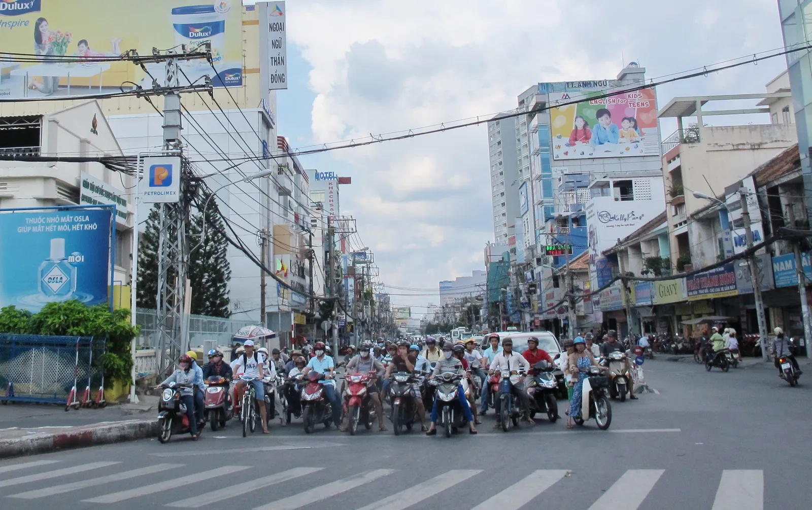Motorbikes waiting at a busy crossing with billboards and tall buildings behind