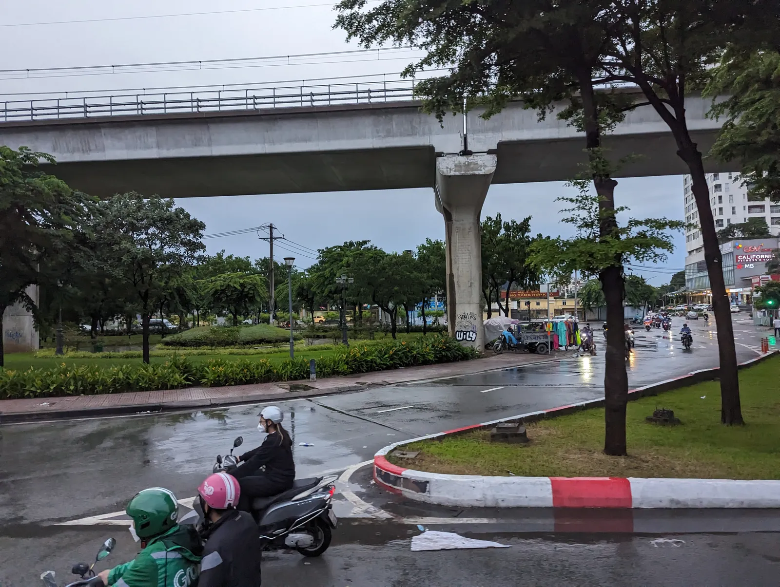 Wet road bend with riders in raincoats under a metro viaduct
