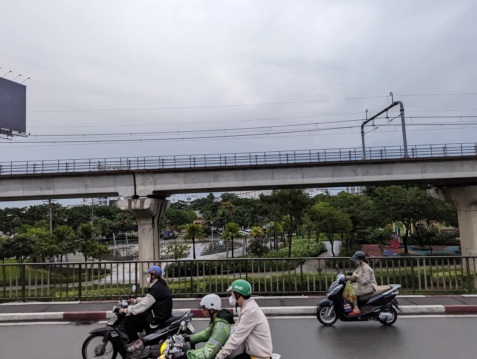 Scooters on a wet road below an elevated road under an overcast sky
