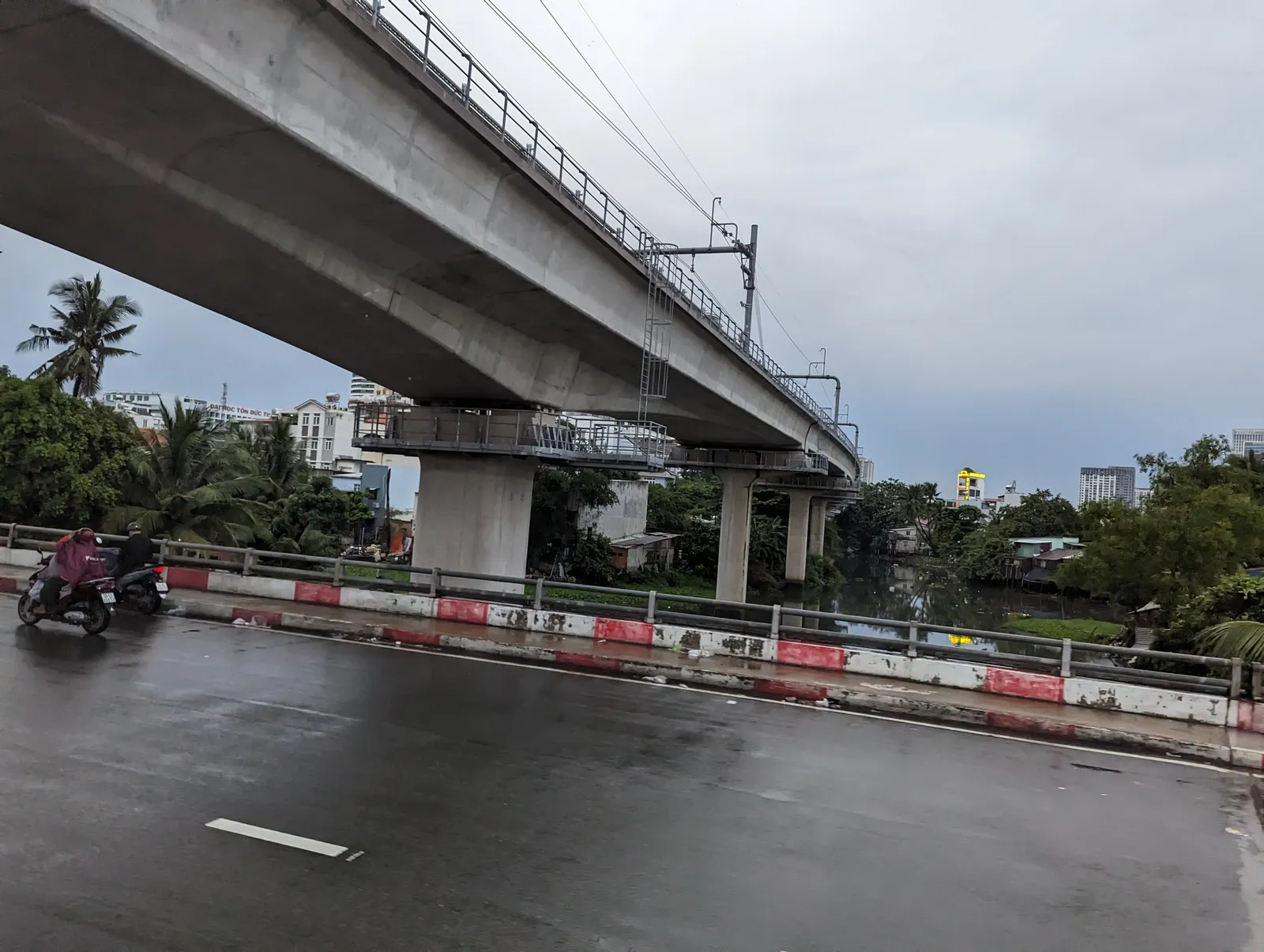 Empty wet road beside a metro viaduct under a grey sky