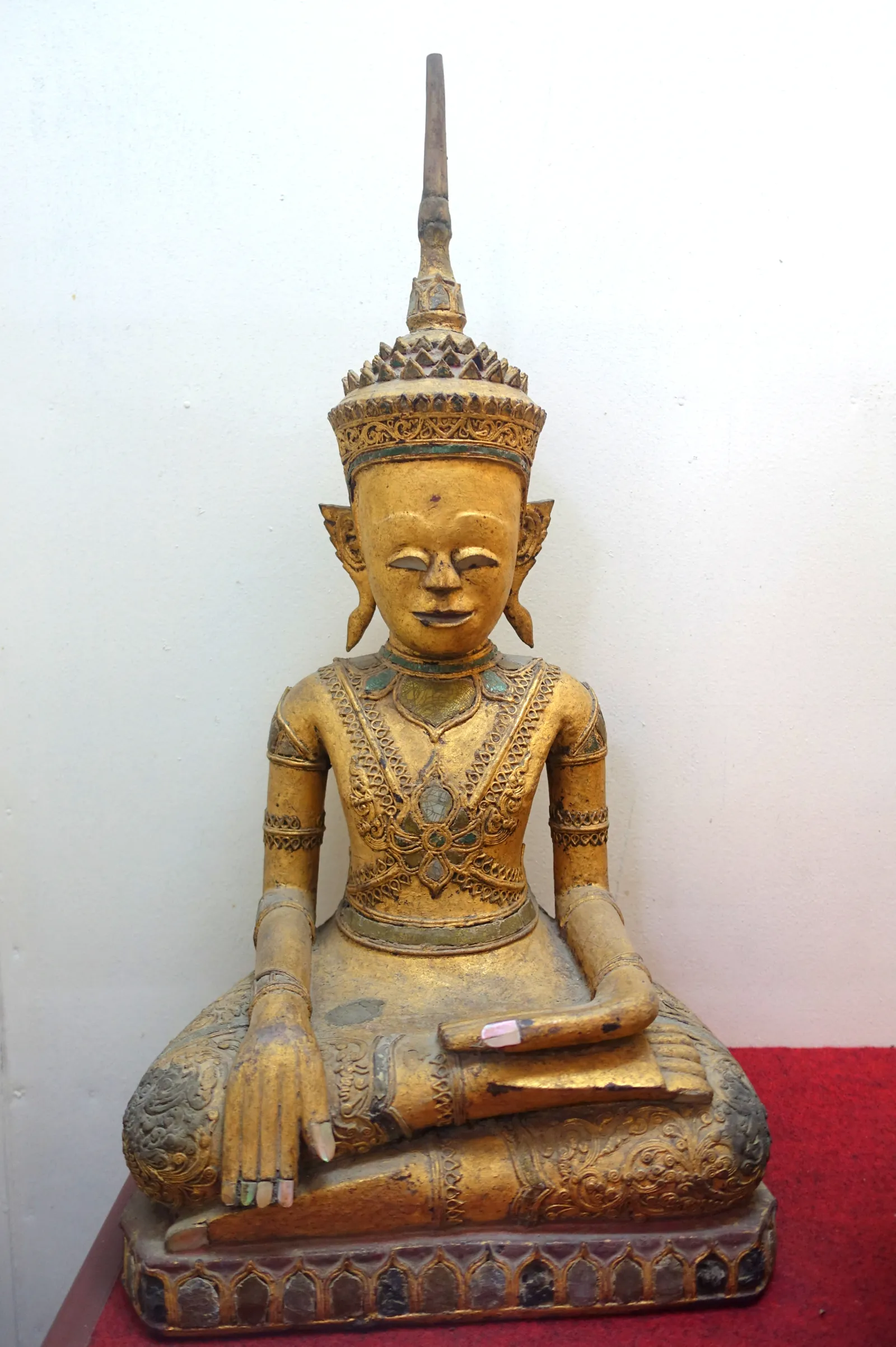 Seated gilded wooden Buddha with a pointed crown on a red cloth base