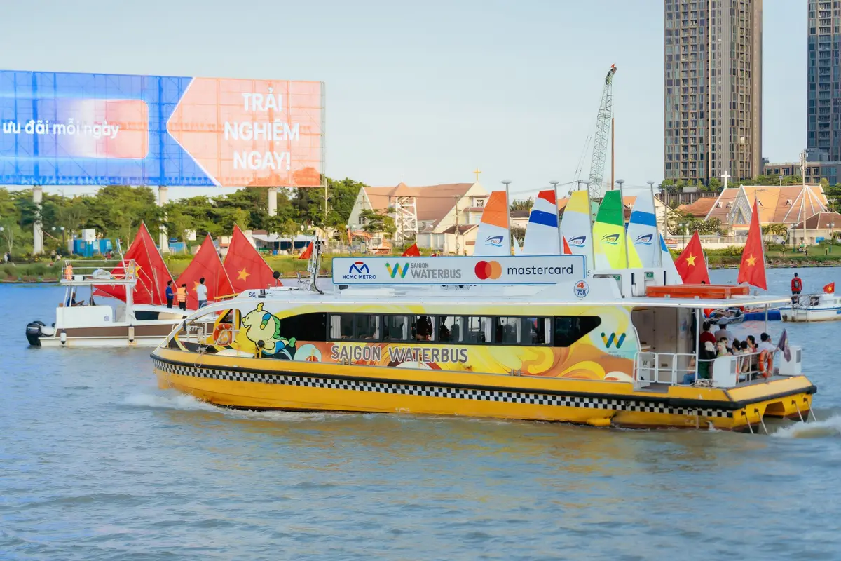 Yellow and white waterbus with flags on the river and a high-rise building behind