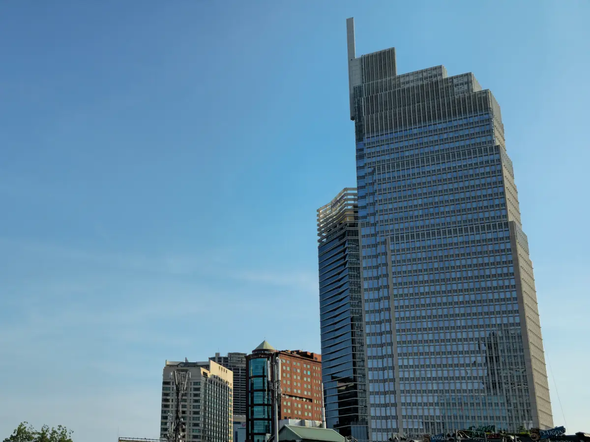 Dark glass tower rising above older buildings under a blue sky.