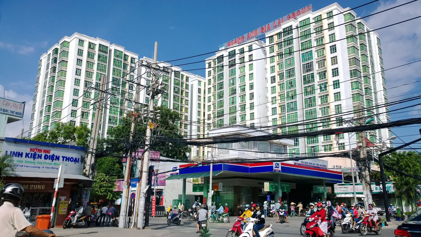 Green and white apartment blocks above a street with a fuel station and motorbikes