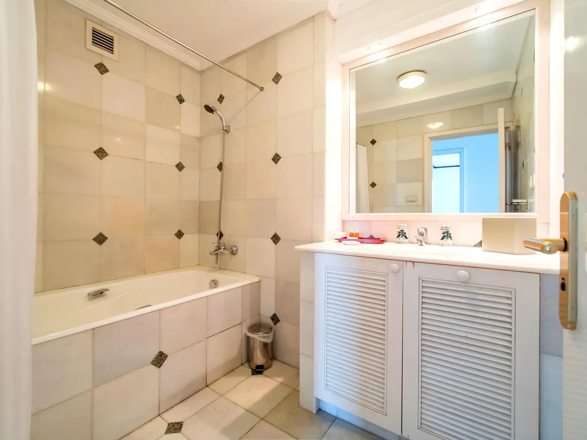Tiled bathroom with a bathtub, shower, vanity and louvred cabinet doors